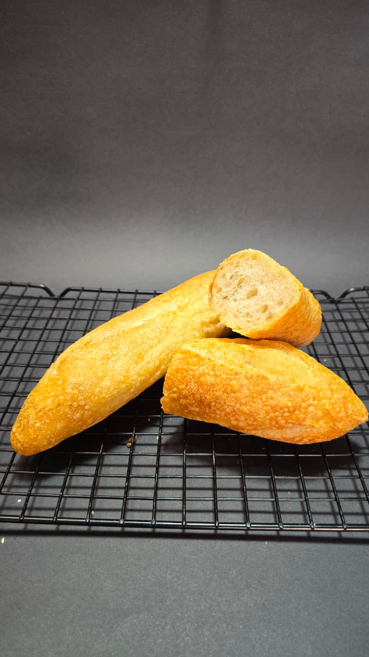 Baguetes artesanais douradas, uma delas cortada mostrando o miolo